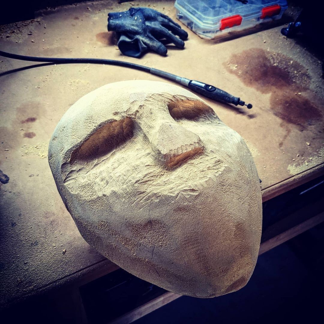Unfinished hand-carved slasher-style mask by Jared Carves on a maker's workbench